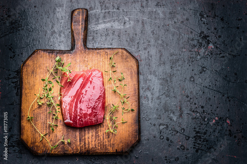 Tuna steak for grill or  frying on wooden cutting board and dark rustic  background with fresh herbst, top view, close up. Seafood concept photo