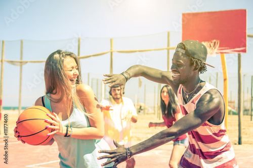 Group of multiracial happy teenagers playing basketball outdoors photo