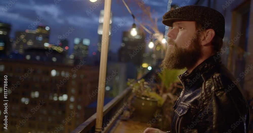 Bearded man in leather jacket and flat cap drinking beer alone on balcony at night in Downtown Los Angeles, California. Recorded in slow motion at 60fps. Bearded man in leather jacket and flat cap drinking beer alone on balcony at night in Downtown Los Angeles, California. Recorded in slow motion at 60fps.