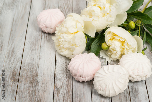 Beautiful white peonies flowers and marshmallows on white wooden background.