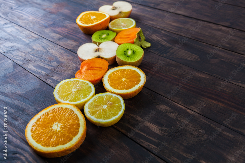 Slices of healthy fruits on dark rustic wooden table. Apple, orange, lemon, kiwi and persimmon with copy space Slices of healthy fruits on dark rustic wooden table. Apple, orange, lemon, kiwi and persimmon with copy space