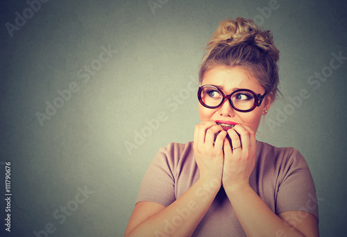 nervous stressed young nerdy woman in glasses biting fingernails looking anxiously photo