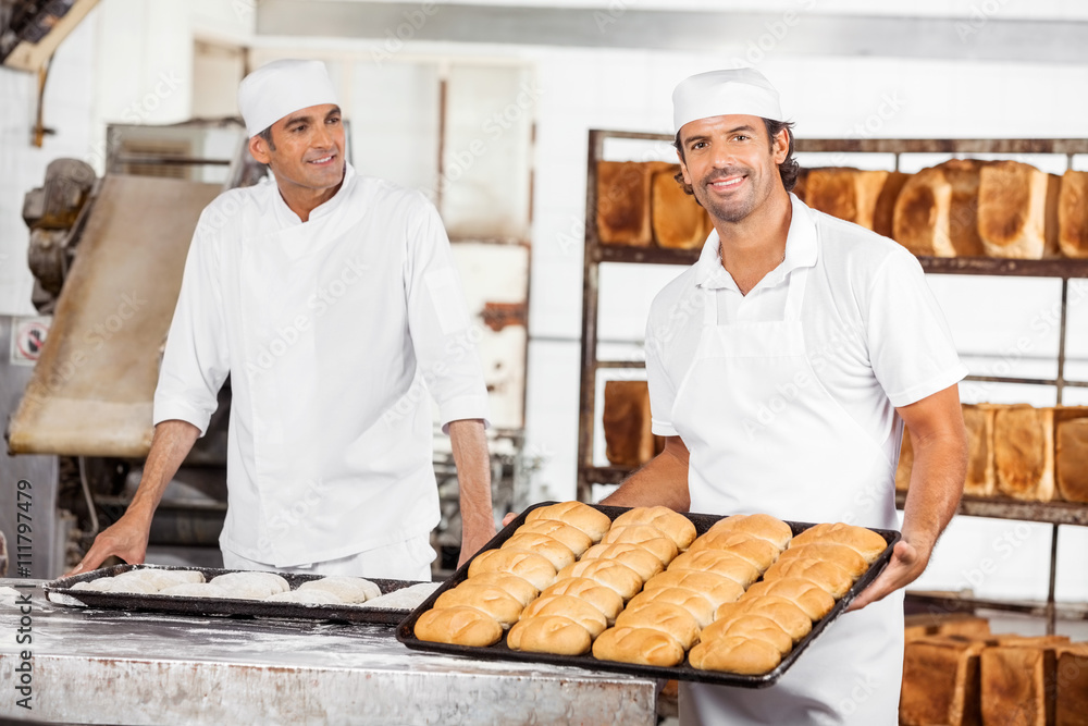 Smiling Baker Showing Breads In Baking Tray By Colleague
