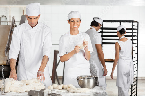 Female Baker Kneading Dough With Colleague In Bakery