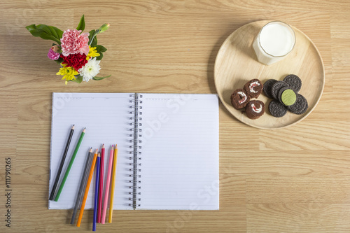 A color pencils and notebook on table . Flowers and milk with co