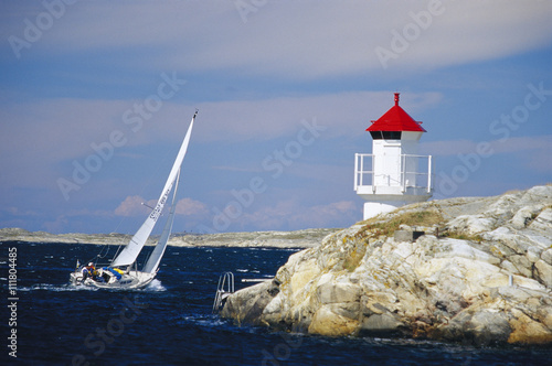 Sailing-boat on the ocean, lighthouse on a rock, Vastkusten, Sweden. photo