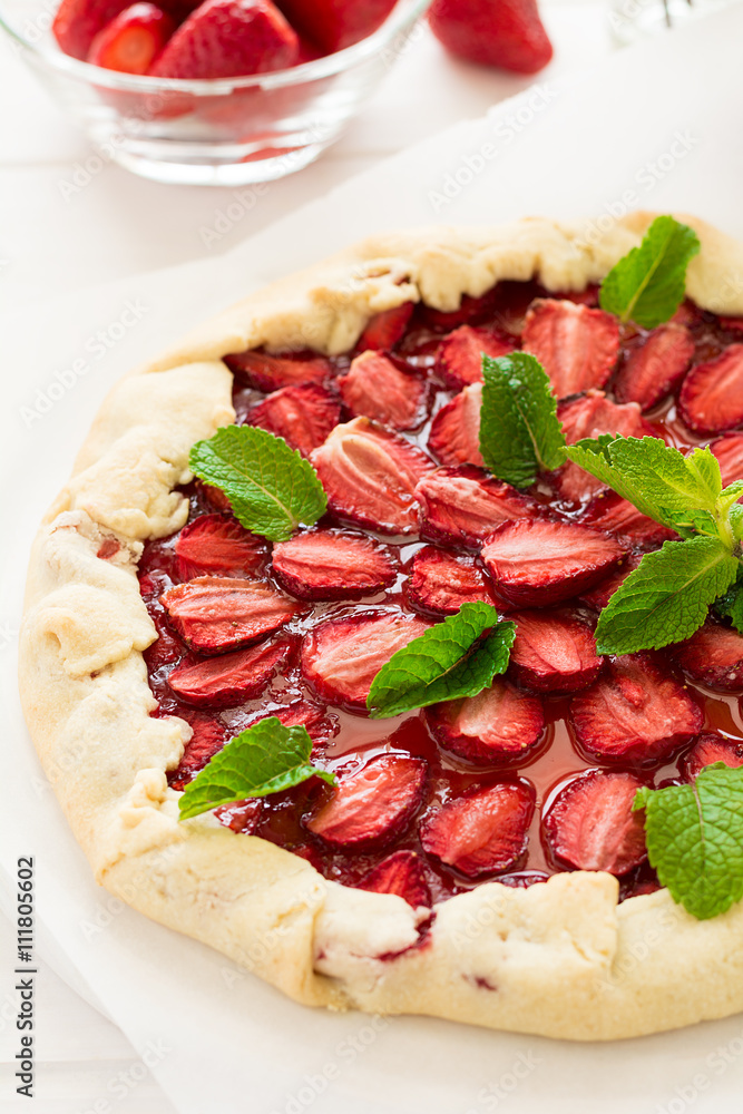 Homemade strawberry galette decorated mint leaves on white wooden background