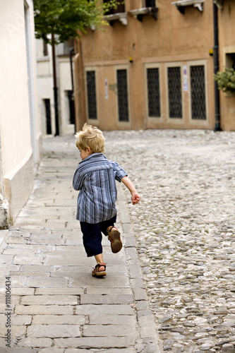 A very young boy running away from the photographer.