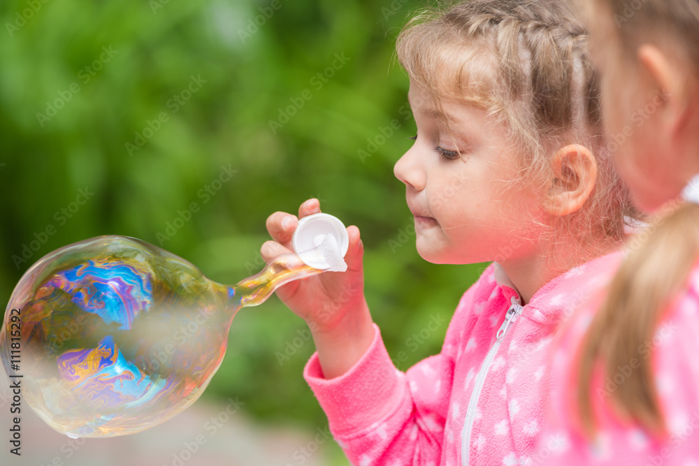 Five-year girl inflates a large bubble, another girl with interest looks at her Five-year girl inflates a large bubble, another girl with interest looks at her