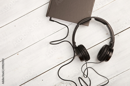Audio book concept with black book and headphones on white wood