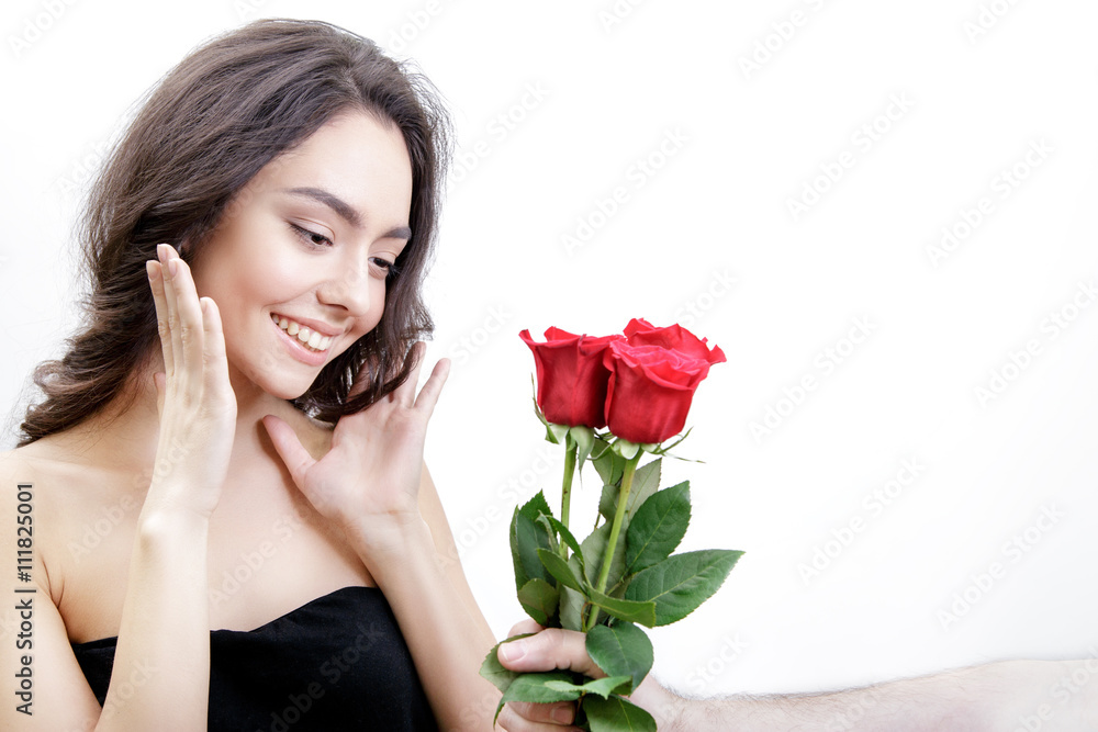Beautiful girl receives three red roses. She is surprised, looking at the flowers and smiling. Men's hand holding three roses. Girl is white with bushy brown hair. Isolated on white background. Beautiful girl receives three red roses. She is surprised, looking at the flowers and smiling. Men's hand holding three roses. Girl is white with bushy brown hair. Isolated on white background.