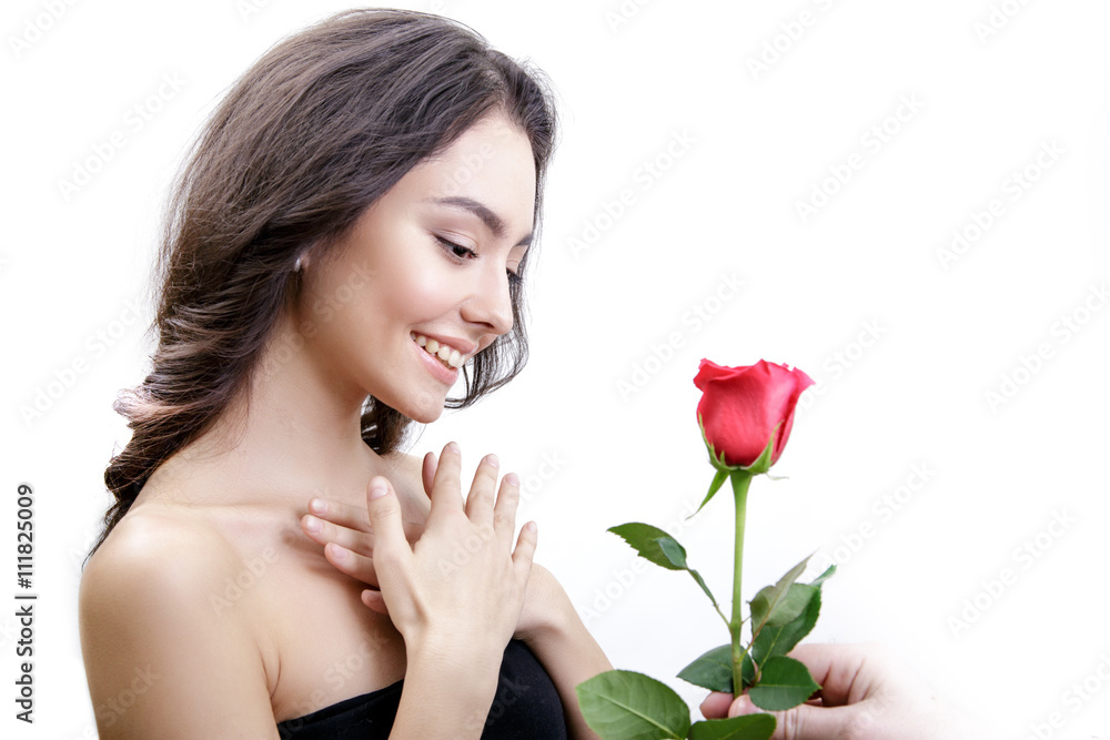 Beautiful angry girl receives one red rose. She is surprised, looking at the flowers and smiling. Men's hand holding one rose. Girl is white with bushy brown hair. Isolated on white background. Beautiful angry girl receives one red rose. She is surprised, looking at the flowers and smiling. Men's hand holding one rose. Girl is white with bushy brown hair. Isolated on white background.