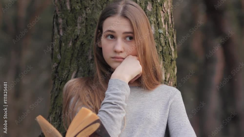 Teenager girl reading classic book leaning against tree trunk in forest in early spring, leisure activity studying outdoor nature park concept Teenager girl reading classic book leaning against tree trunk in forest in early spring, leisure activity studying outdoor nature park concept