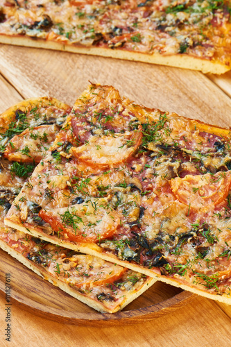 Cut traditional pizza with mushrooms, cheese and tomatoes sprinkled with herbs on wooden plate