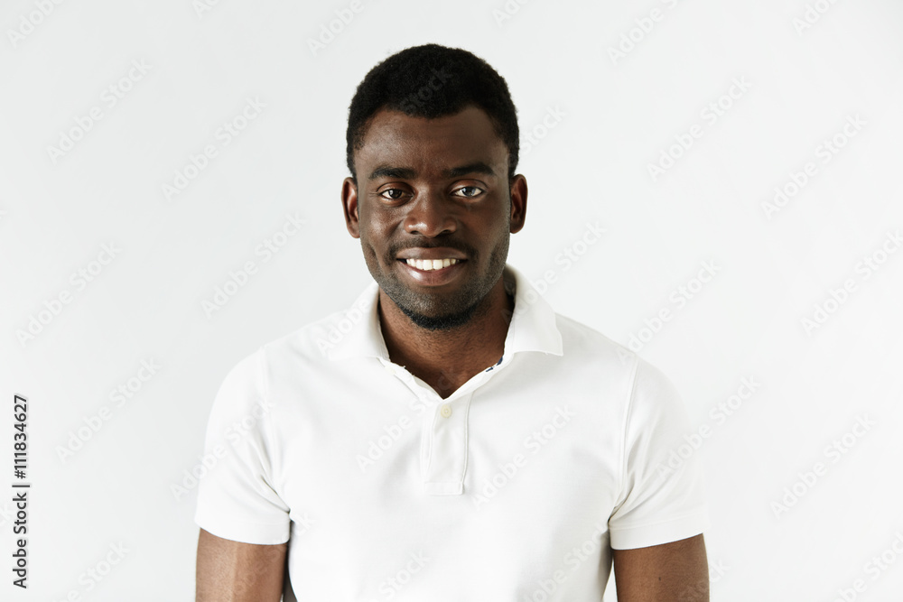 Close up of successful young black entrepreneur wearing white polo shirt looking and smiling at the camera with winning happy expression, achieving business goals. Success and achievement concept Close up of successful young black entrepreneur wearing white polo shirt looking and smiling at the camera with winning happy expression, achieving business goals. Success and achievement concept