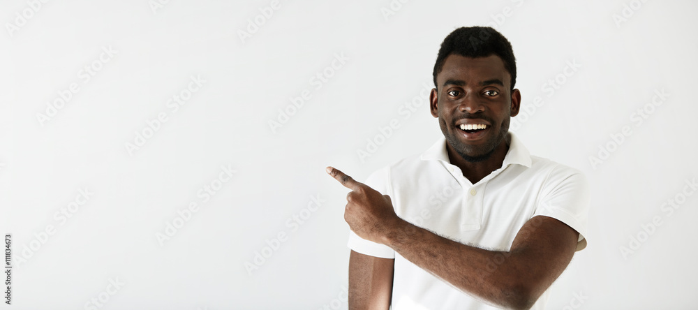 Cheerful young black man smiling and pointing at the copy space for ...