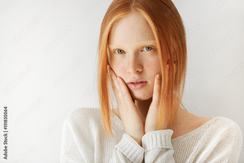 Close up shot of cute redhead teenage girl with perfect freckled skin and blue eyes wearing casual clothes, with hands on her cheeks, looking at the camera with serious expression on her face Close up shot of cute redhead teenage girl with perfect freckled skin and blue eyes wearing casual clothes, with hands on her cheeks, looking at the camera with serious expression on her face