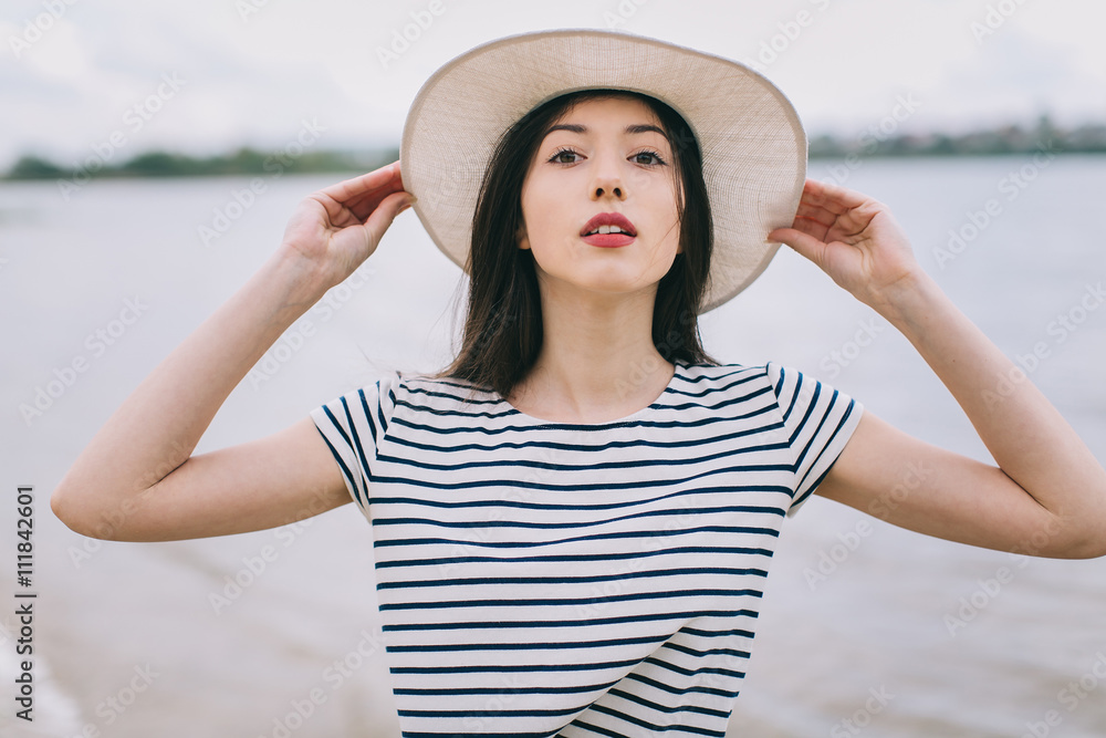 Beautiful stylish and fashionable girl in a hat posing on a beach.