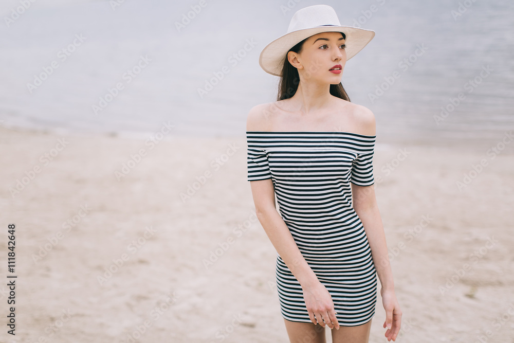 Beautiful stylish and fashionable girl in a hat posing on a beach.