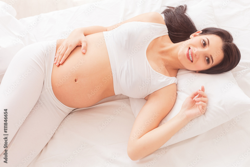 Cute pregnant woman is relaxing in bedroom Cute pregnant woman is relaxing in bedroom