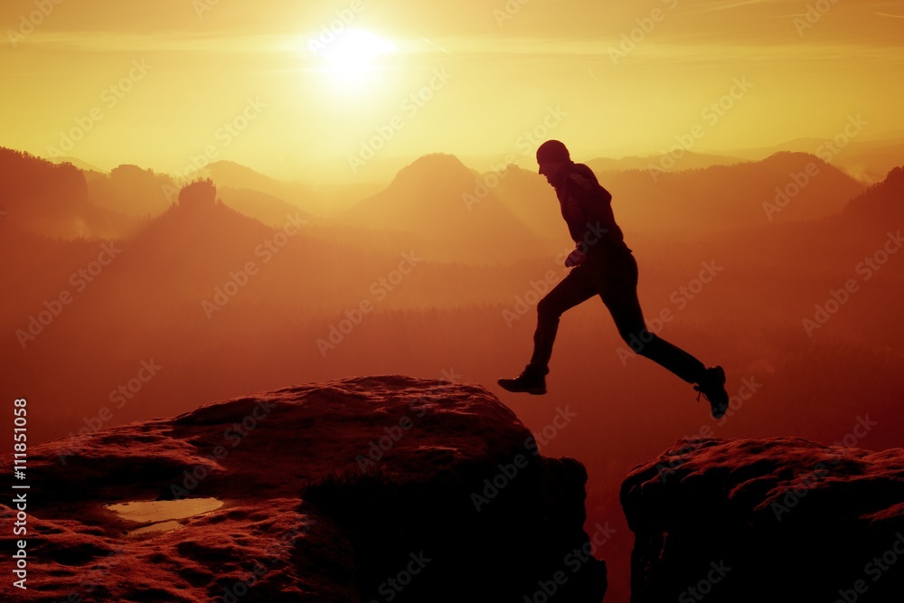 Young crazy man jump on mountain peak. Silhouette of jumping man
