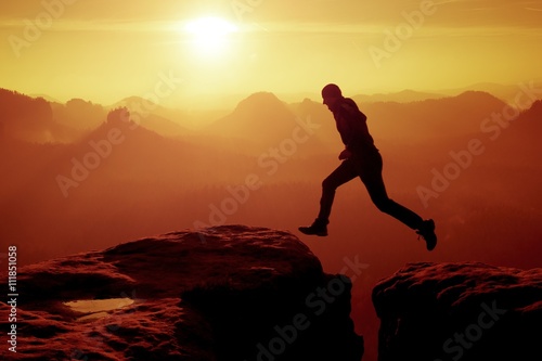 Young crazy man jump on mountain peak. Silhouette of jumping man photo