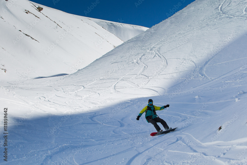 Man snowboarder snowboarding on fresh white snow on ski slope on Sunny winter day