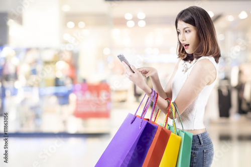 Woman shopping in shopping mall and use mobile phone shopping and find promotion.