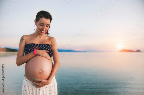 Young happy pregnant woman at the beach at sunset. Lens flare effect