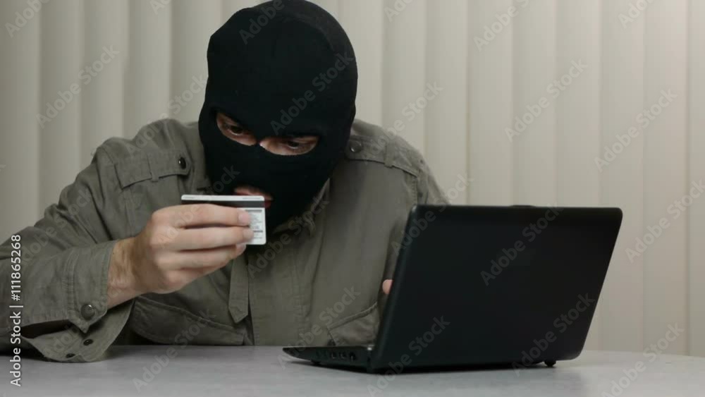 Hacker with a black mask using a stolen credit card to buy online with a stolen laptop. Great video for and project involving cyber criminality and thief Hacker with a black mask using a stolen credit card to buy online with a stolen laptop. Great video for and project involving cyber criminality and thief