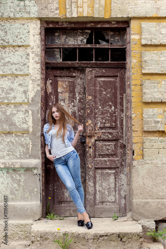 beautiful young sweet girl with red hair in jeans standing near the door of the old city