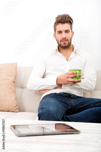 A young adult man sitting on couch with coffee..