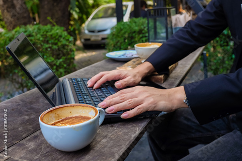 Business asian man black suit using laptop with cup of coffee on