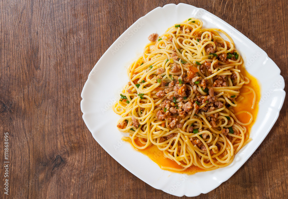 spaghetti with vegetables and minced meat in a plate on wooden table