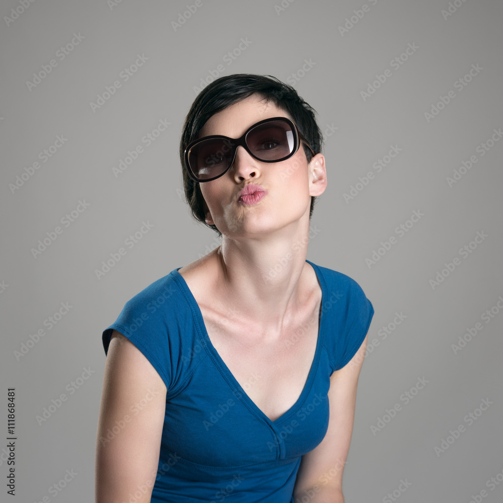 Cute charming short hair woman wearing sunglasses blowing air kiss at camera over gray studio background. Cute charming short hair woman wearing sunglasses blowing air kiss at camera over gray studio background.