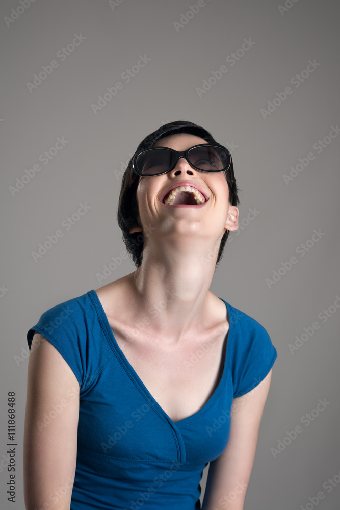 Laughing young short hair cutie wearing sunglasses over gray studio background. Laughing young short hair cutie wearing sunglasses over gray studio background.
