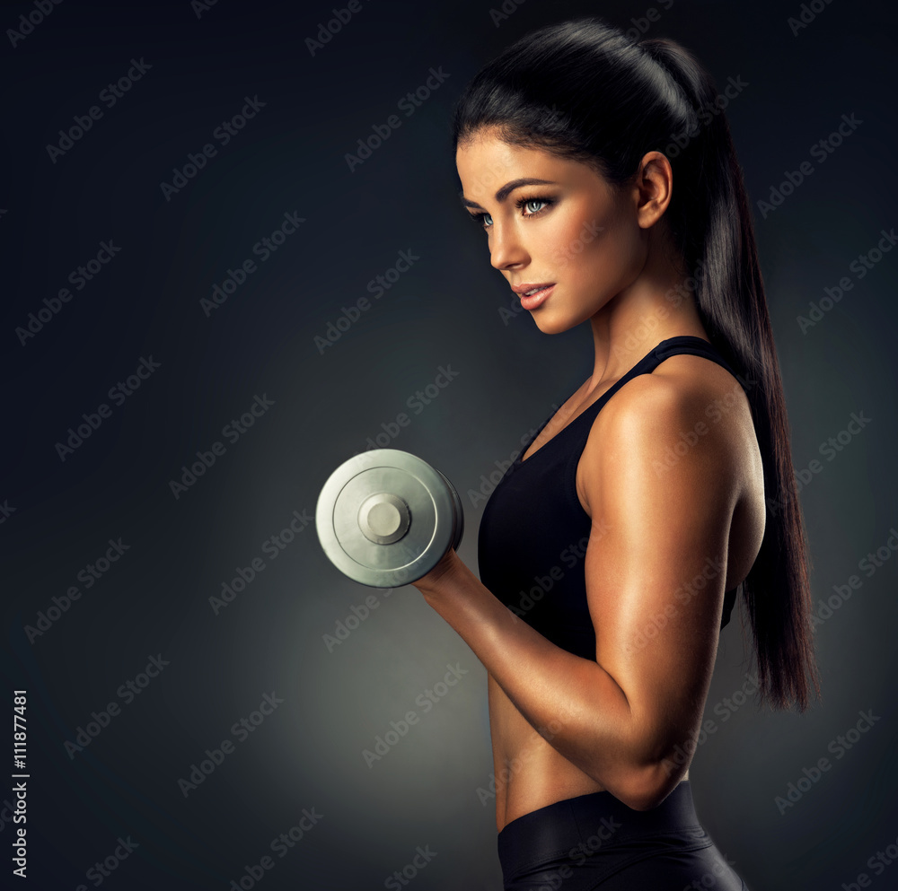 Beautiful fitness woman lifting dumbbells . Fitness sporty woman showing  her well trained body . A beautiful girl's body with rippling muscles from  strength training . Photos | Adobe Stock