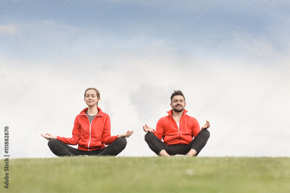 Evening yoga on background of beautiful sky. Man and woman meditating in mountains. People relax at sunset.
