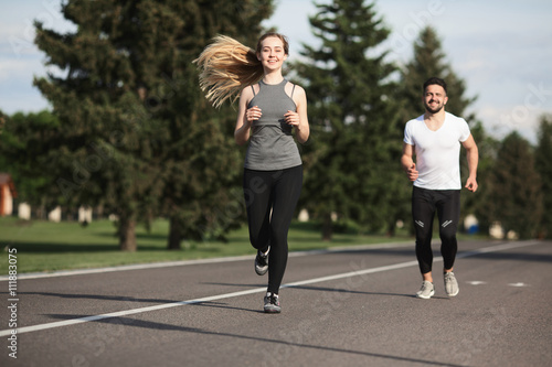 Closeup portrait of sport woman jogging along road with her partner or boyfriend running on background. Fitness, sport and lifestyle concepts.