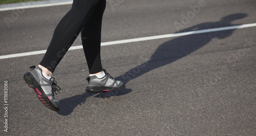 Jogging woman on track. Legs of woman running on road near park or forest. Closeup of female in running shoes going for run on road at sunrise or sunset.