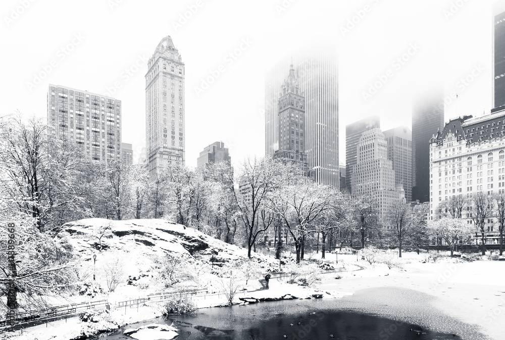 Naklejka premium Staw w Central Parku w mglisty zimowy poranek, jak widać z Gapstow Bridge. Niskie chmury pokrywają wieżowce Manhattanu