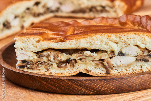 A piece of pie with a filling of chicken and mushrooms lying on a wooden plate