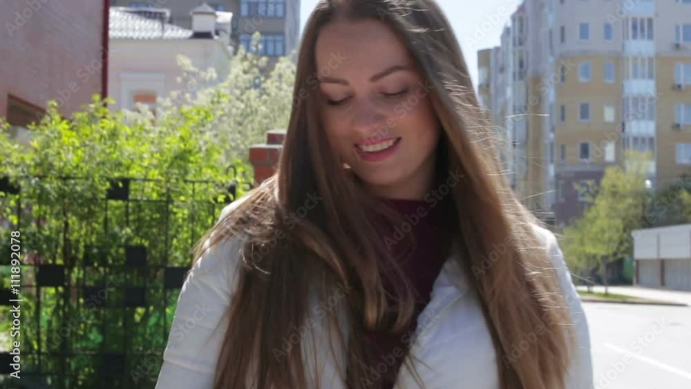 Beautiful young girl writes a message to use a smartphone walking down the street in the summer and smiling Beautiful young girl writes a message to use a smartphone walking down the street in the summer and smiling
