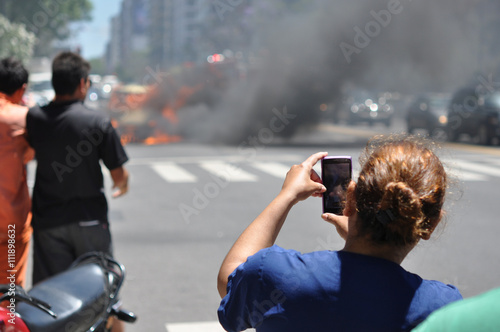 Zuschauerin benutzt Handy um brennendes Auto mitten auf der Straße in Buenos Aires, Argentinien zu filmen