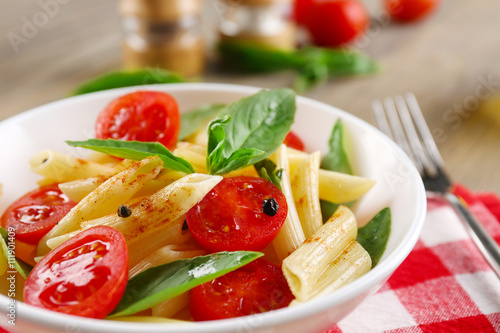 Plate of pasta with cherry tomatoes and basil leaves on table closeup