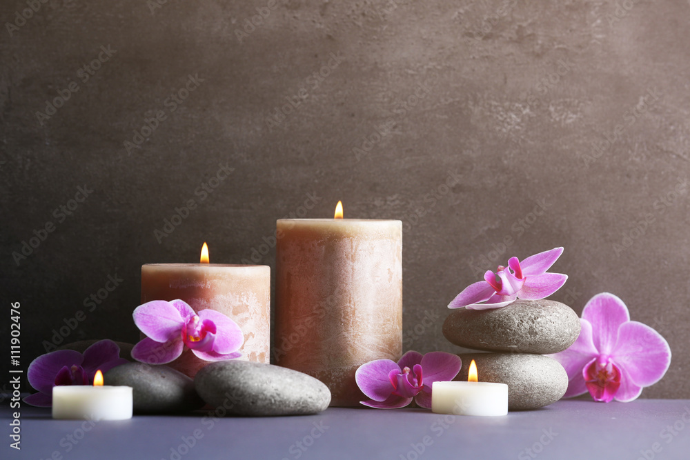 Composition of spa pebbles, flowers and candles on grey background Composition of spa pebbles, flowers and candles on grey background