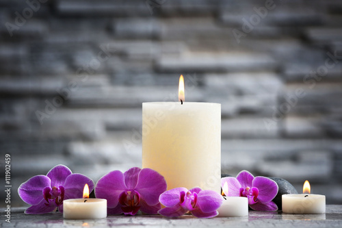 Composition of aroma candles and beautiful flowers on grey brick wall background