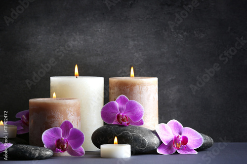 Composition of spa pebbles, flowers and candles on grey background