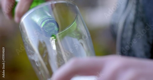 Close up on Caucasian man's hands pouring beer from a generic green bottle into a tall glass at an urban party.  Recorded in slow motion at 60fps.