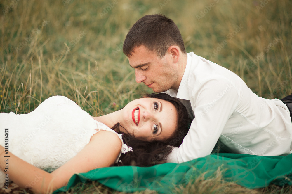 Happy wedding couple lying on green grass at the summer time Happy wedding couple lying on green grass at the summer time